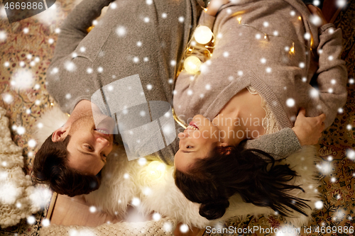 Image of happy couple with garland lying on floor at home