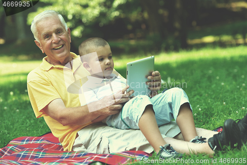 Image of grandfather and child in park using tablet