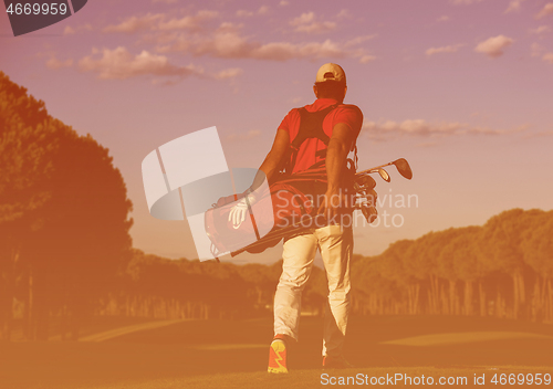 Image of golfer  walking and carrying golf  bag