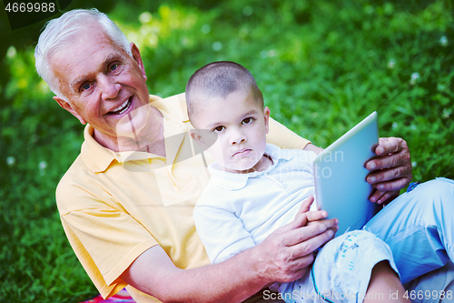 Image of grandfather and child in park using tablet