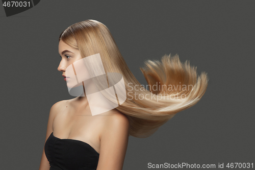 Image of Beautiful model with long smooth, flying blonde hair isolated on dark studio background.