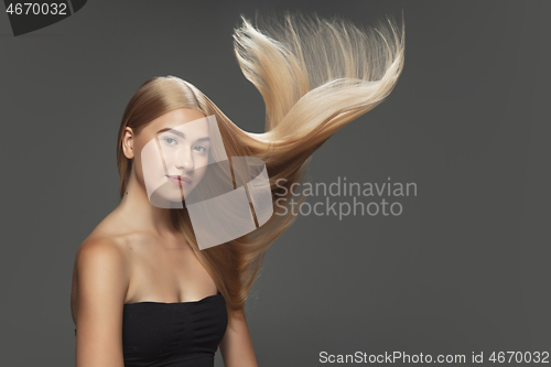 Image of Beautiful model with long smooth, flying blonde hair isolated on dark studio background.