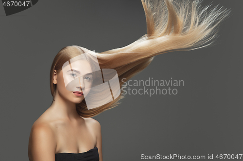 Image of Beautiful model with long smooth, flying blonde hair isolated on dark studio background.