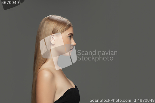 Image of Beautiful model with long smooth, flying blonde hair isolated on dark studio background.