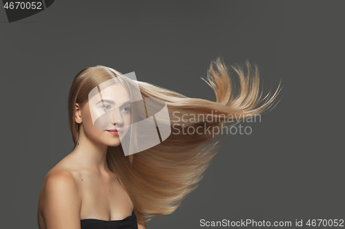 Image of Beautiful model with long smooth, flying blonde hair isolated on dark studio background.