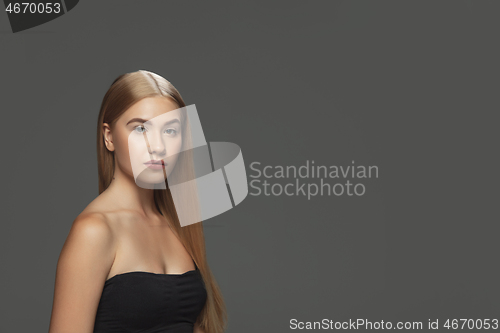 Image of Beautiful model with long smooth, flying blonde hair isolated on dark studio background.