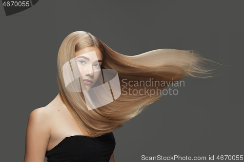 Image of Beautiful model with long smooth, flying blonde hair isolated on dark studio background.