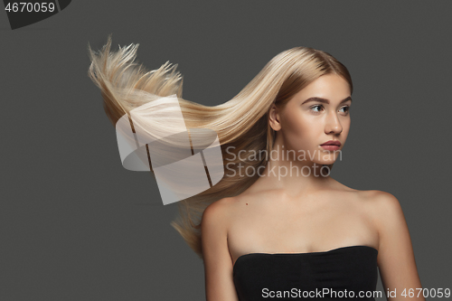 Image of Beautiful model with long smooth, flying blonde hair isolated on dark studio background.