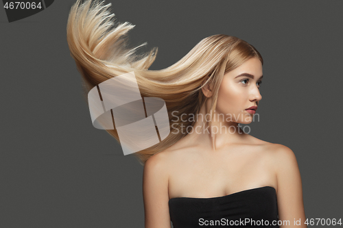 Image of Beautiful model with long smooth, flying blonde hair isolated on dark studio background.