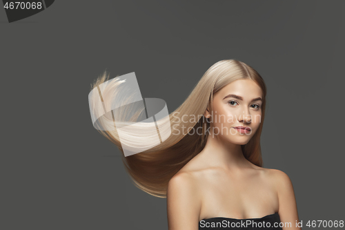 Image of Beautiful model with long smooth, flying blonde hair isolated on dark studio background.