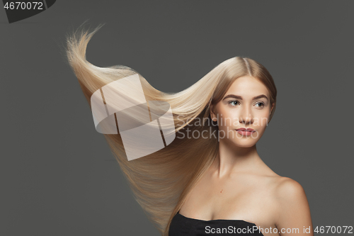 Image of Beautiful model with long smooth, flying blonde hair isolated on dark studio background.