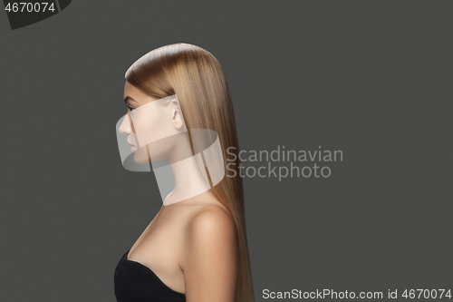 Image of Beautiful model with long smooth, flying blonde hair isolated on dark studio background.