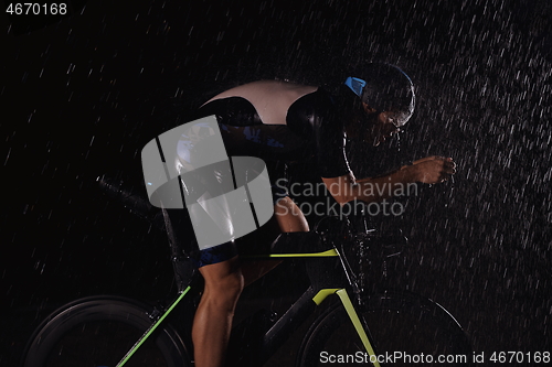 Image of triathlon athlete riding bike fast on rainy night