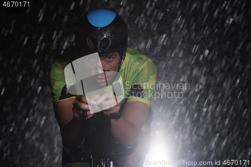 Image of triathlon athlete riding bike fast on rainy night