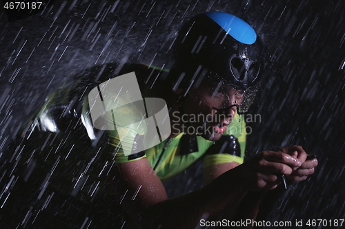 Image of triathlon athlete riding bike fast on rainy night