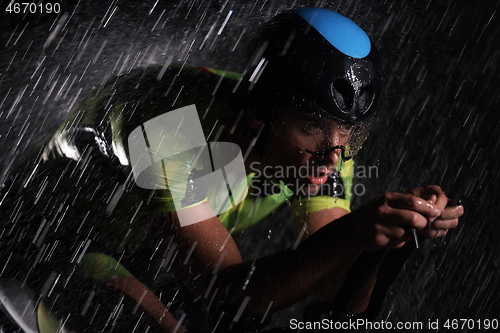 Image of triathlon athlete riding bike fast on rainy night