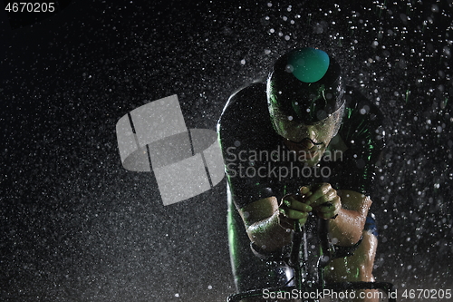 Image of triathlon athlete riding bike fast on rainy night