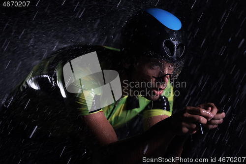 Image of triathlon athlete riding bike fast on rainy night