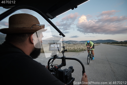 Image of videographer taking action shot of triathlon athlete while riding bike