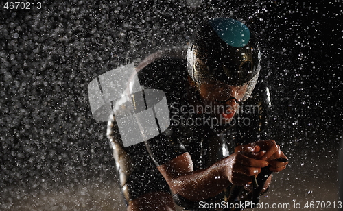 Image of triathlon athlete riding bike fast on rainy night