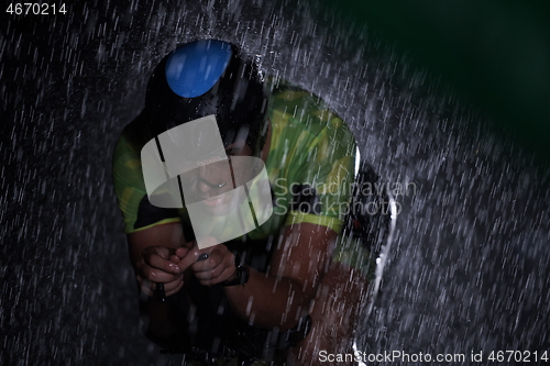 Image of triathlon athlete riding bike fast on rainy night