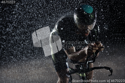 Image of triathlon athlete riding bike fast on rainy night