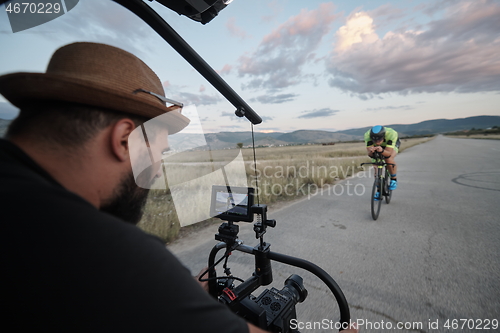 Image of videographer taking action shot of triathlon athlete while riding bike