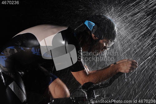 Image of triathlon athlete riding bike fast on rainy night