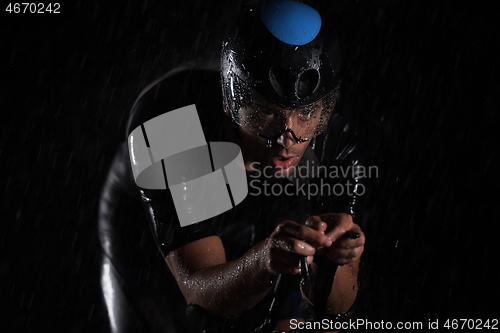 Image of triathlon athlete riding bike fast on rainy night