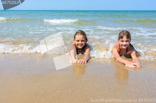 Image of Girls lie on the sand of the sea coast and happily look at the frame