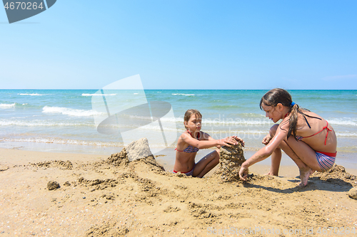 Image of Two girls play in the sand on the beach of the sea coast