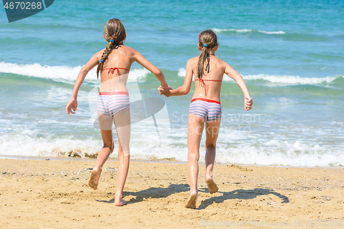 Image of Two little sisters running to swim in the sea, back visas