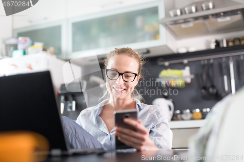 Image of Stay at home and social distancing. Woman in her casual home clothing working remotly from kitchen dining table. Video chatting using social media with friend, family, business clients or partners