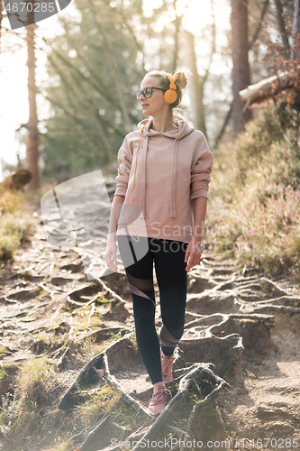 Image of Active sporty woman listening to the music while hiking in autumn fall forest. Female jogger training outdoor. Healthy lifestyle image of young caucasian woman walking on hiking trail in nature