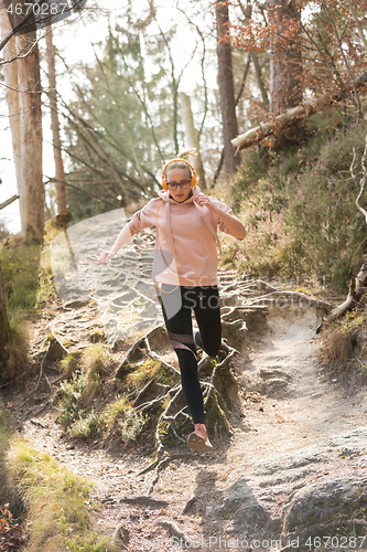 Image of Active sporty woman running in autumn fall forest jumping over the roots on the path. Healthy lifestyle image of young active caucasian woman jogging outside in nature