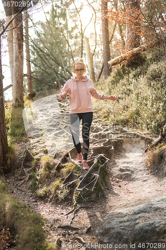 Image of Active sporty woman listening to the music while running in autumn fall forest. Female runner training outdoor. Healthy lifestyle image of young caucasian woman jogging outside