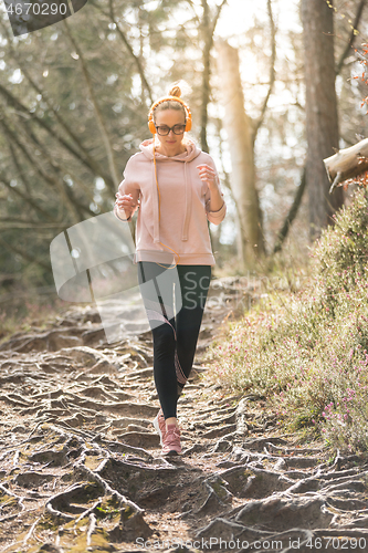 Image of Active sporty woman listening to the music while running in autumn fall forest. Female runner training outdoor. Healthy lifestyle image of young caucasian woman jogging outside