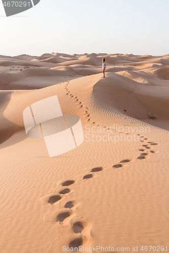 Image of Blonde female Caucasian traveler leaving footprints in sand dunes when walking in dessert in Oman