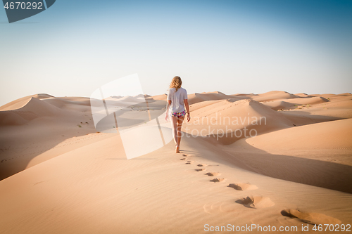 Image of Blonde female Caucasian traveler leaving footprints in sand dunes when walking in dessert in Oman