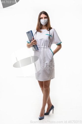 Image of Girl in medical clothes and mask posing with tablet on white background