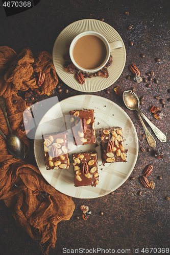 Image of Chocolate cake with caramel frosting, pecans and hot coffee, on rustic background. Freshly baked