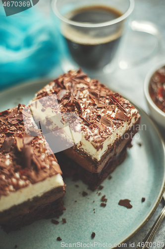 Image of Delicious chocolate cake with layers served on ceramic blue plate. With cup of fresh black coffe