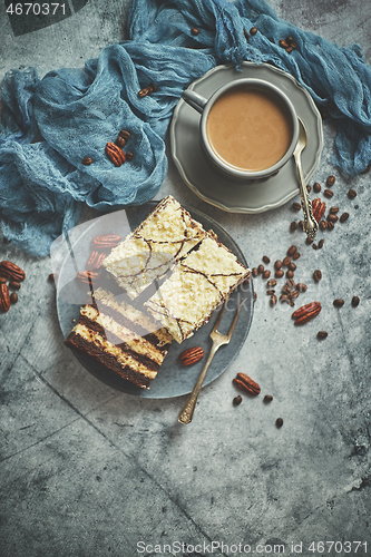 Image of Tasty layered cake sprinkled with white chocolate. Served with cup of coffee on a gray concrete