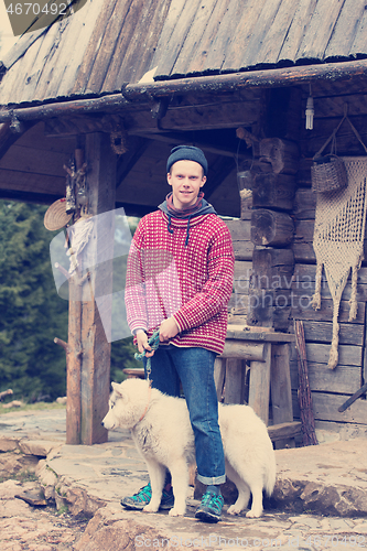 Image of young hipster with dog in front of wooden house