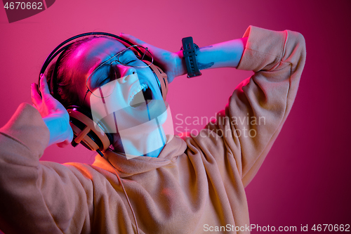 Image of Fashion pretty woman with headphones listening to music over neon background