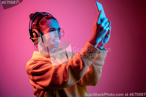 Image of Fashion pretty woman with headphones listening to music over neon background