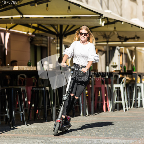 Image of Trendy fashinable teenager girls riding public rental electric scooters in urban city environment. New eco-friendly modern public city transport in Ljubljana, Slovenia