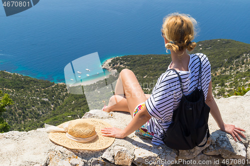 Image of Active sporty woman on summer vacations sitting on old stone wall at Lubenice village, wearing straw hat and beach backpack enjoying beautiful coastal view of Cres island, Croatia