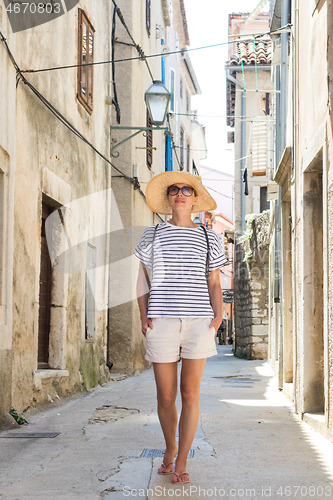 Image of Beautiful blonde young female traveler wearing straw sun hat sightseeing and enjoying summer vacation in an old traditional costal town at Adriatic cost, Croatia