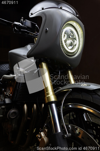 Image of Custom caferacer motorbike on dark background with its headlight on.